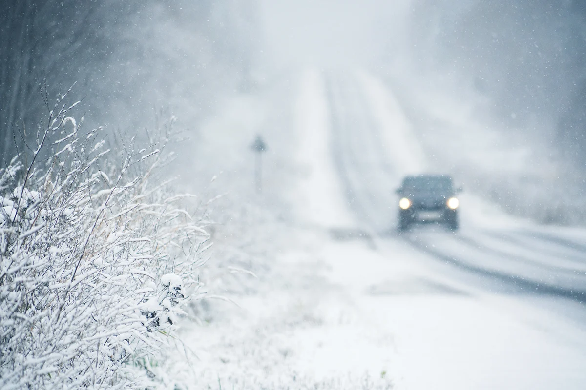 image of vehicle driving on a snowy road with snow in the air.