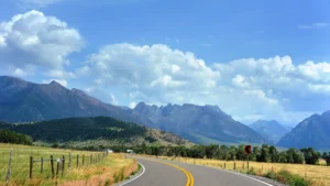 Big Sky summer activities 2026 could include scenic drives down curving roads such as this one pictured against a backdrop of mountains, white clouds, and big blue sky
