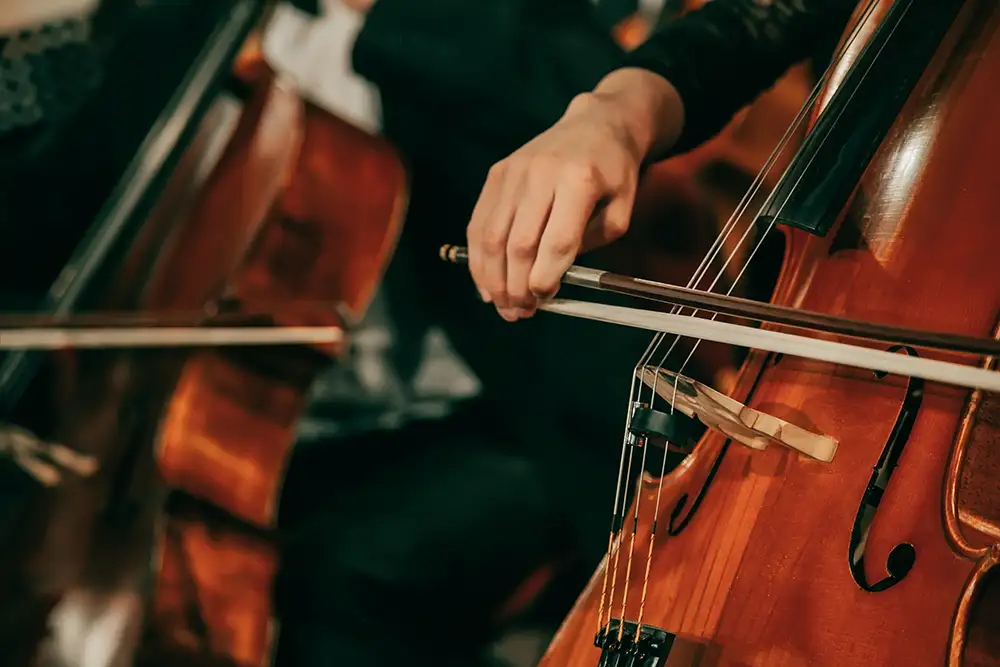 Symphony orchestra on stage, hands playing cello. Shallow depth of field, vintage style.